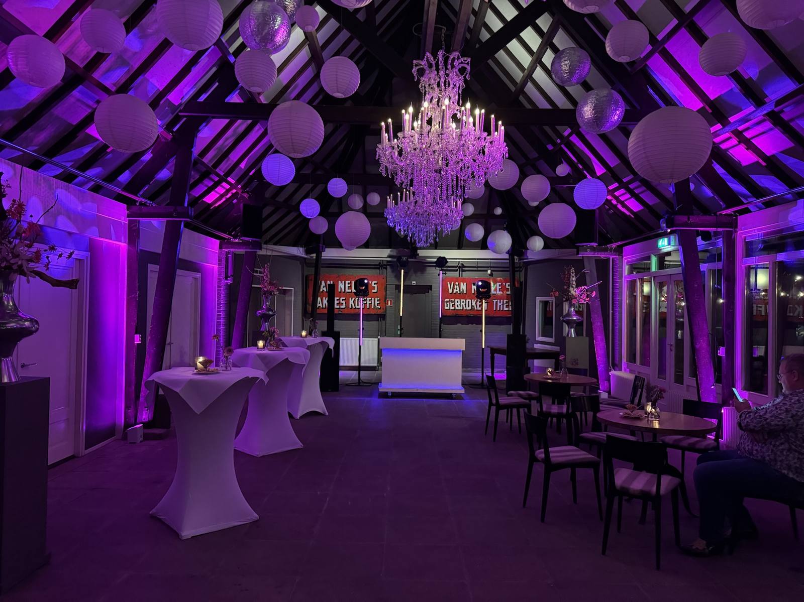 DJ Remy Flier achter de witte DJ-booth in een sfeervol paars verlichte trouwzaal met kroonluchter