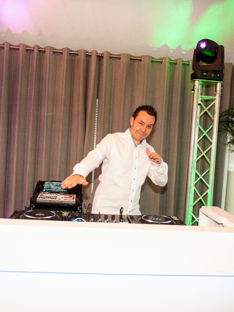 Bruiloft-DJ Remy achter de witte DJ-booth tijdens een feest